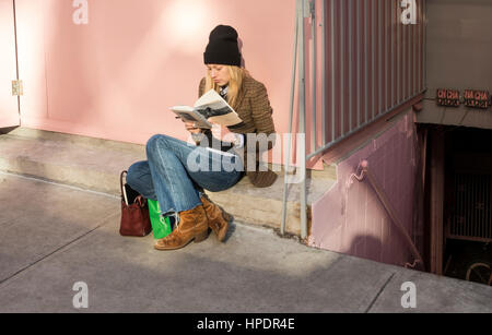 Elegante giovane donna leggendo una copertina rigida libro mentre in attesa di un tavolo in un ristorante Foto Stock