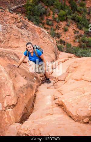 Una giovane donna escursionista sospende la sua salita fino a rosso roccia di sorridere alla telecamera. Prese sulla Cattedrale di famose rock escursione a Sedona, in Arizona. Foto Stock