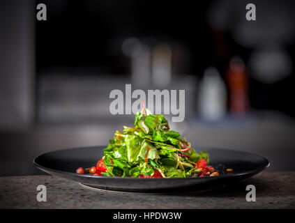 La vitamina a molla insalata fresca di lattuga, melograno, pompelmo e dadi in piastra nera. Cucina interna in background Foto Stock