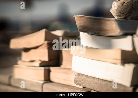 Molti vecchi libri in brossura su un tavolo in legno da spiaggia tenuta giù con pietre dal vento. Foto Stock