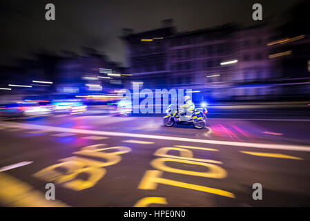 Una moto di polizia che corre a un incidente di notte lungo Whitehall, Londra, Regno Unito, con luci blu lampeggiante. Sfocatura movimento. Unità di polizia a velocità Foto Stock