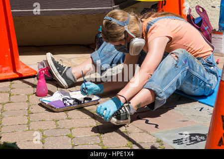 Giovane donna / artista indossare un respiratore di protezione durante la pittura a mano Arte / decorazioni su un marciapiede Foto Stock