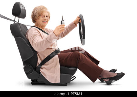 Gioiosa donna anziana tenendo premuto un tasto auto e seduto nel sedile di un'auto isolati su sfondo bianco Foto Stock