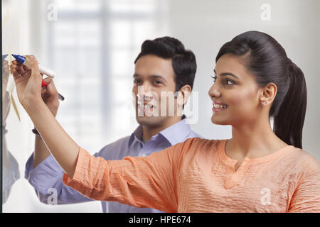 Due colleghi sorridente in ufficio scrivendo su una lavagna bianca Foto Stock