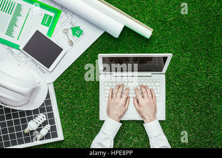 Progetto di casa, pannello solare, casco e ingegnere di lavoro con un laptop sull'erba verde edificio sostenibile e le energie alternative concept Foto Stock