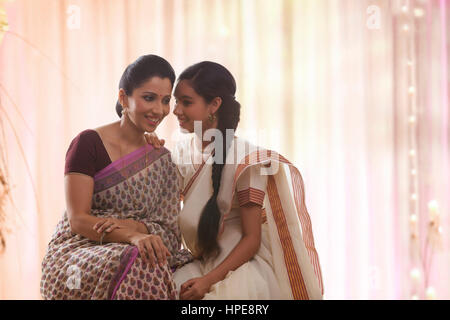 Sorridente figlia adolescente in sari whispering a madre Foto Stock