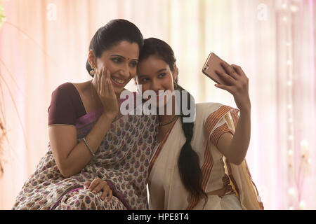 Sorridente figlia adolescente in sari e madre tenendo selfie Foto Stock