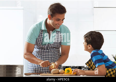 Padre sbucciare le patate in cucina mentre si parla al suo figlio Foto Stock