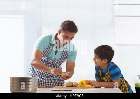 Padre sbucciare le patate in cucina mentre suo figlio osserva Foto Stock