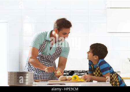 Padre sbucciare le patate in cucina mentre si parla al suo figlio Foto Stock