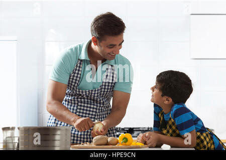 Padre sbucciare le patate in cucina mentre si parla al suo figlio Foto Stock