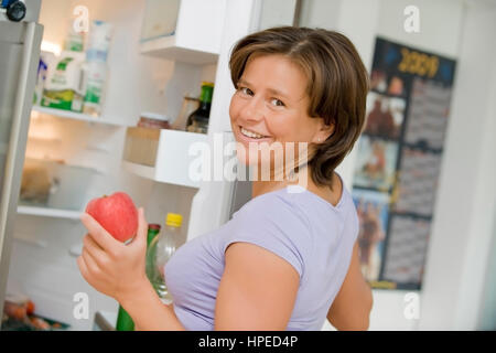 Modello rilasciato , Junge, lachende Frau nimmt Apfel aus dem Kuehlschrank - donna con un Apple in mano Foto Stock