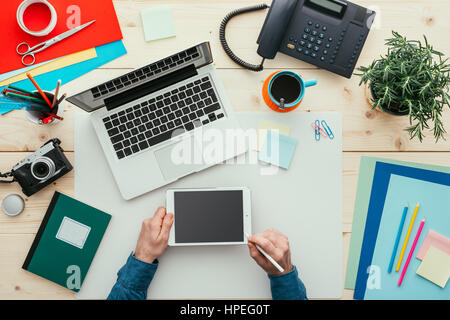 Creative designer freelance lavorare alla scrivania nel suo ufficio, egli è abbozzare utilizzando una tavoletta e una penna stylus, vista dall'alto Foto Stock