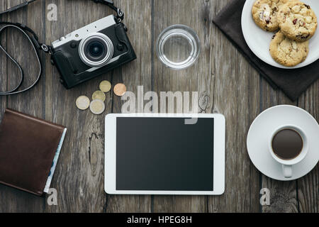 Fotocamera vintage, tablet, una tazza di caffè e biscotti su una scrivania in legno, rilassante colazione al concetto di casa Foto Stock