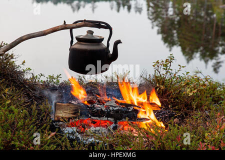 Stagno annerito Bollitore acqua bollente su fiamme dal fuoco durante la passeggiata lungo il lago Foto Stock