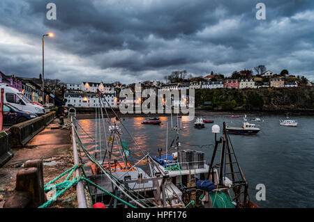 Portree Harbour, Isola di Skye in Scozia al crepuscolo. Febbraio 2017, mostra gli edifici al crepuscolo come le luci si accendono, impostare contro scure nuvole drammatico. Foto Stock