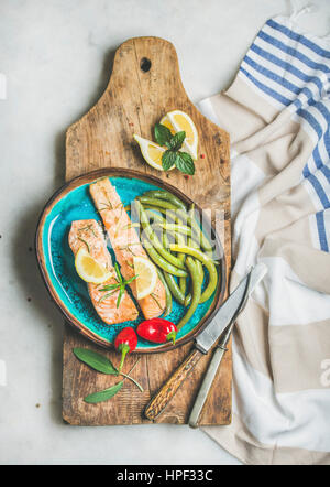 Forno arrosto di filetto di salmone con limone e rosmarino, peperoncino, affogò fagioli verdi in ceramica blu della piastra sulla tavola di legno su marmo grigio Sfondo, Foto Stock