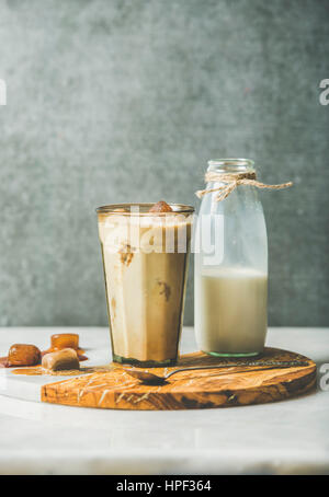 Iced caramello latte estate cocktail di caffè con latte e caffè congelato di cubetti di ghiaccio nel bicchiere a servire in legno di olivo e marmo scheda sopra tabella grigia, scuro Foto Stock