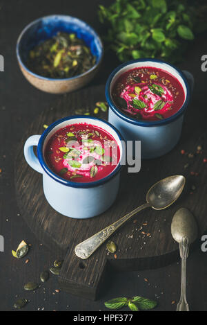 Primavera detox zuppa di barbabietole con la menta, pistacchio, chia, lino e i semi di zucca in smalto blu tazze su legno scuro dello sfondo. Pulire, mangiare sano, Foto Stock