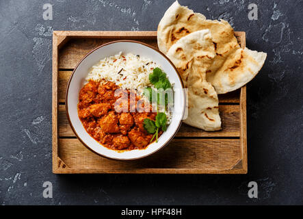 Pollo Tikka masala curry piccante alimenti a base di carne con riso e fresca pane naan nel vassoio in legno nero su sfondo di pietra Foto Stock