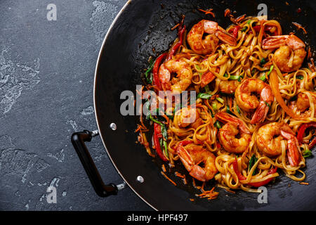 Udon friggere gli spaghetti con i gamberi nel wok padella in pietra scura sullo sfondo close up Foto Stock
