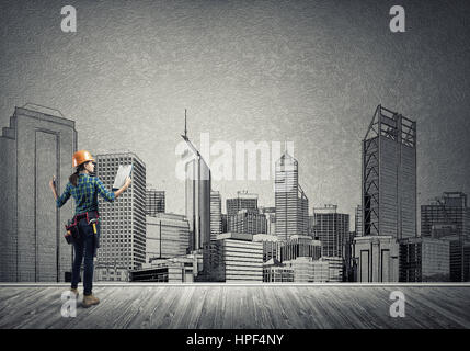 Vista posteriore di ingegnere di donna con la cartella e schizzi di progetto di costruzione sulla parete Foto Stock