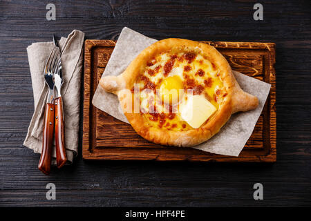 Ajarian Khachapuri in stile georgiano tradizionale formaggio sulla pasta nero bruciato sullo sfondo di legno Foto Stock