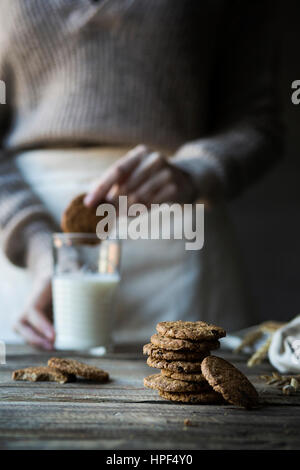 Biscotti di cereali sul tavolo di legno e la donna immergendo un biscotto in un bicchiere di latte Foto Stock