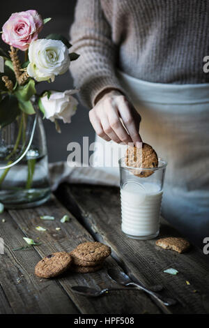 Donna immergendo un biscotto in un bicchiere di latte Foto Stock