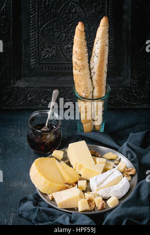 Il piatto di formaggi. Assortimento varietà di formaggio con le noci, marmellata e pane su vintage piastra metallica con tessili su blu scuro con canvas black ornato bac Foto Stock