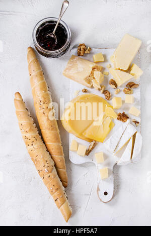 Il piatto di formaggi. Assortimento di formaggi con noci, marmellata e pane in legno bianco che serve scheda sopra in calcestruzzo bianco sullo sfondo di texture. Vista da sopra con uno spazio Foto Stock