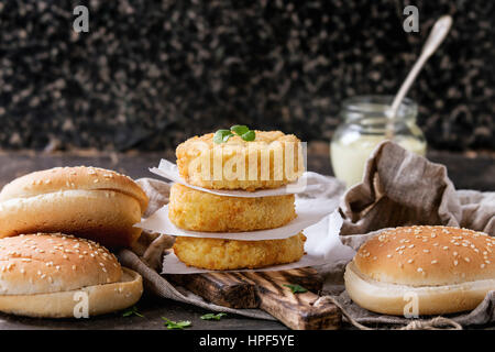 Ingredienti per rendere vegan burger. Veggie il formaggio e la cipolla cotolette, salsa di yogurt, hamburger bunsand erbe , servita su tavola di legno con tessili su Foto Stock