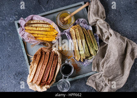 Varietà di fettine di american ombre cioccolato, tè verde Matcha e curcuma frittelle servita in carta involucro di carta con miele salse sul vassoio di legno su b Foto Stock