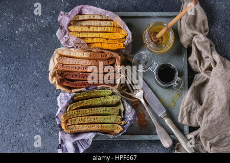 Varietà di fettine di american ombre cioccolato, tè verde Matcha e curcuma frittelle servita in carta involucro di carta con miele salse sul vassoio di legno su b Foto Stock