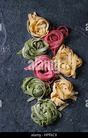 Varietà di colore crudo fresco non cotti pasta fatta in casa tagliatelle spinaci verde, rosa la barbabietola e tradizionale giallo su calcestruzzo scuro dello sfondo. A Foto Stock
