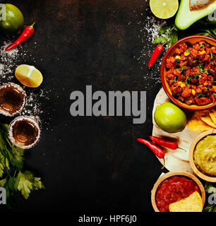 Cibo messicano concetto: tortilla chips, guacamole, salsa chili con fagioli, tequila scatti e ingredienti freschi su vintage metallo arrugginito sfondo. A Foto Stock