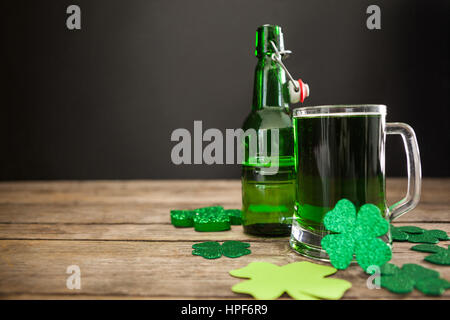 Boccale di birra verde, bottiglia di birra e trifogli per il giorno di San Patrizio sulla tavola di legno Foto Stock