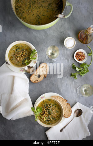 Lentil Verde il cocco la zuppa in ciotole di ceramica servita con pane e vino bianco. Fotografato su sfondo grigio. Foto Stock