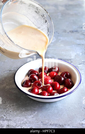 La preparazione di cherry clafoutis.Versare il composto di uova in una padella le ciliege fresche. Foto Stock