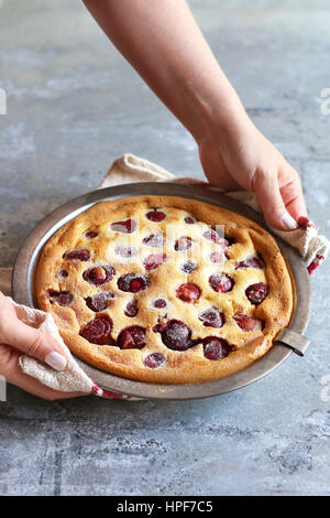 Mani tenendo una padella con appena sfornato clafoutis ciliegia Foto Stock