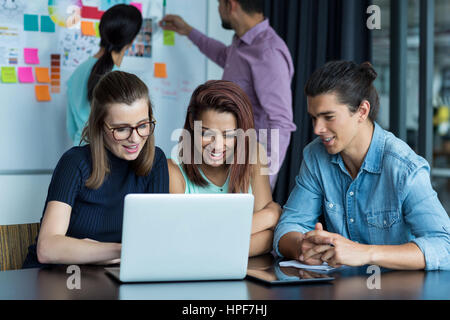 Sorridendo gli imprenditori aventi la discussione su computer portatile in ufficio Foto Stock