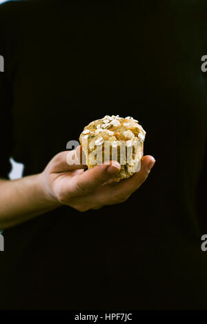 Una donna con il vestito nero tenendo un muffin alla carota fotografata da vista frontale. Foto Stock