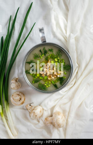 Crema di zuppa di funghi guarnita con noci sbriciolata e erbe tritate fotografato su uno sfondo bianco dalla vista dall'alto. Materie di funghi e verde oni Foto Stock