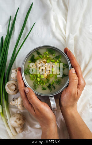 Una donna è in possesso di una ciotola di crema di zuppa di funghi guarnita con noci tritate e le erbe fotografata da vista dall'alto. Materie di cipollotti e funghi Foto Stock