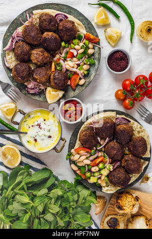 Polpette turche aka koftes servita su pane pita su due piastre di rame con il freddo insalata di fagioli e cipolle rosse fotografata da vista dall'alto. Salsa di yogurt, h Foto Stock
