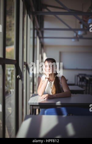 Riflessivo schoolgirl seduta in Aula a scuola Foto Stock