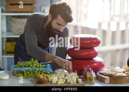 Venditore disponendo formaggio al contatore nel negozio di alimentari Foto Stock