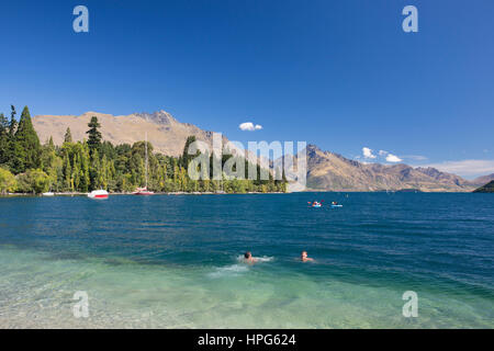 Queenstown, Otago, Nuova Zelanda. Nuotatori sfidando le gelide acque di Queenstown Bay, il lago Wakatipu, Cecil picco e Walter picco in background. Foto Stock