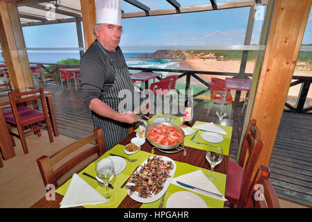 Portogallo: Chef Gabriele con la sua specialità della casa che pongono a decorato tavolo con vista sul mare nel ristorante Gabriel II in Aljezur Foto Stock