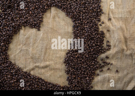 I chicchi di caffè formando forma di cuore sul tessile a sacco Foto Stock